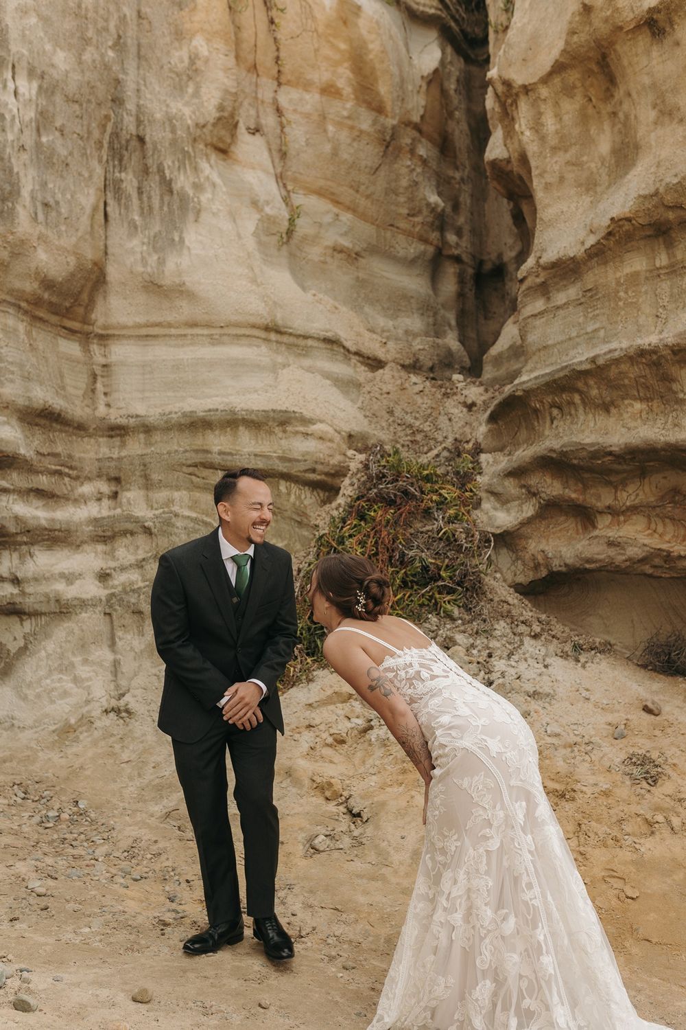 A couple in wedding attire shares a joyful moment against dramatic sandstone cliffs at Calafia Beach Park in San Clemente..