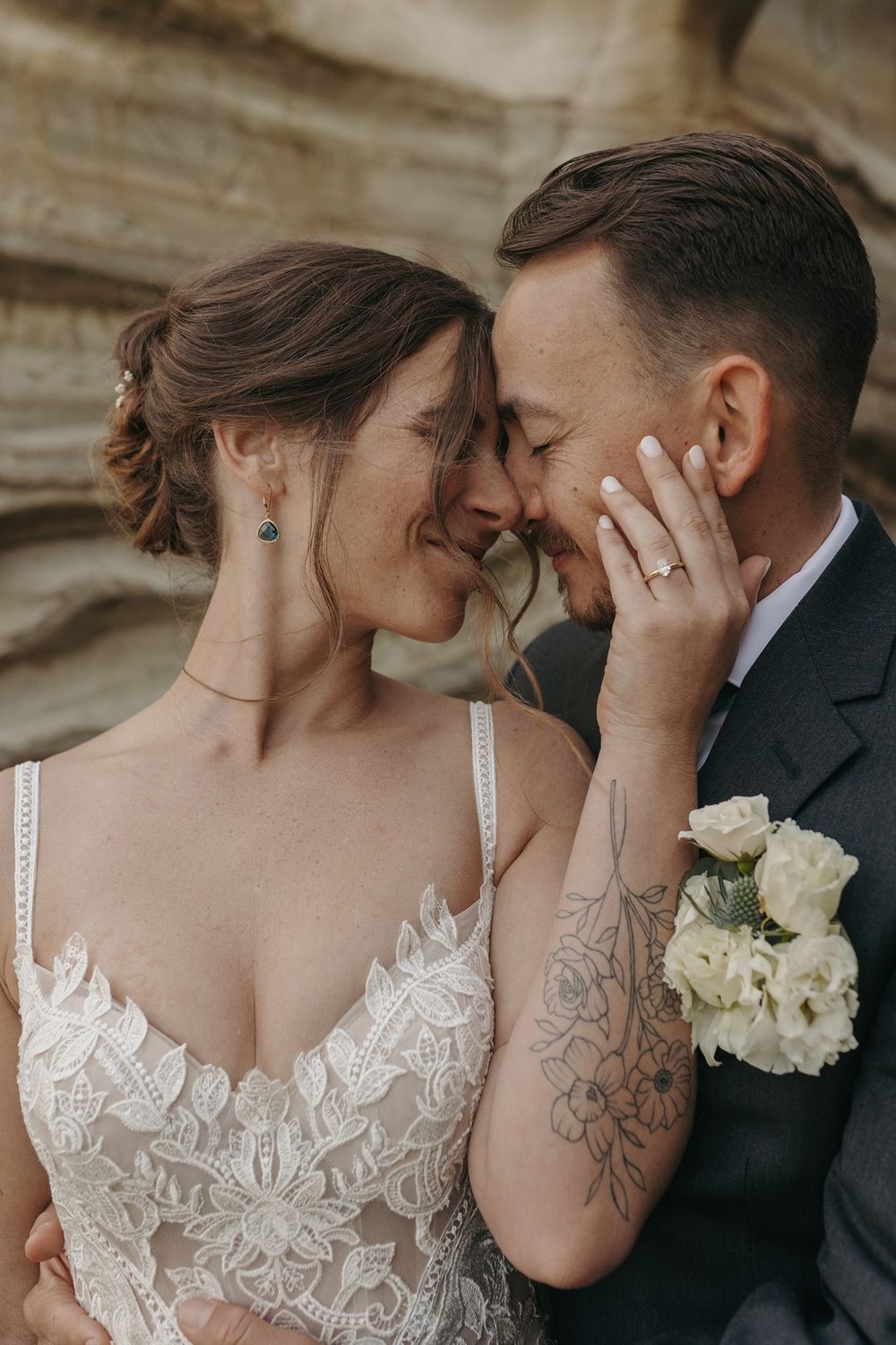 Newlyweds in black suit and white lace dress embrace tenderly against natural stone backdrop at Calafia Beach Park in San Clemente.