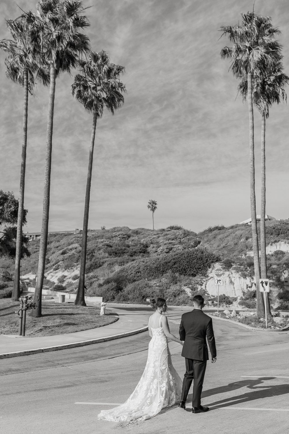 A black and white wedding photo shows a couple walking along a palm tree-lined path at Calafia Beach Park in San Clemente..