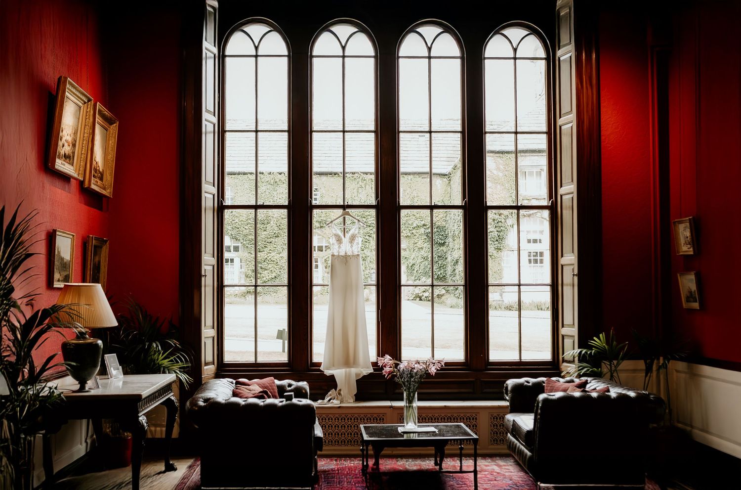 A gothic-style room with tall arched windows, red walls, and vintage furniture creates a dramatic Victorian atmosphere.