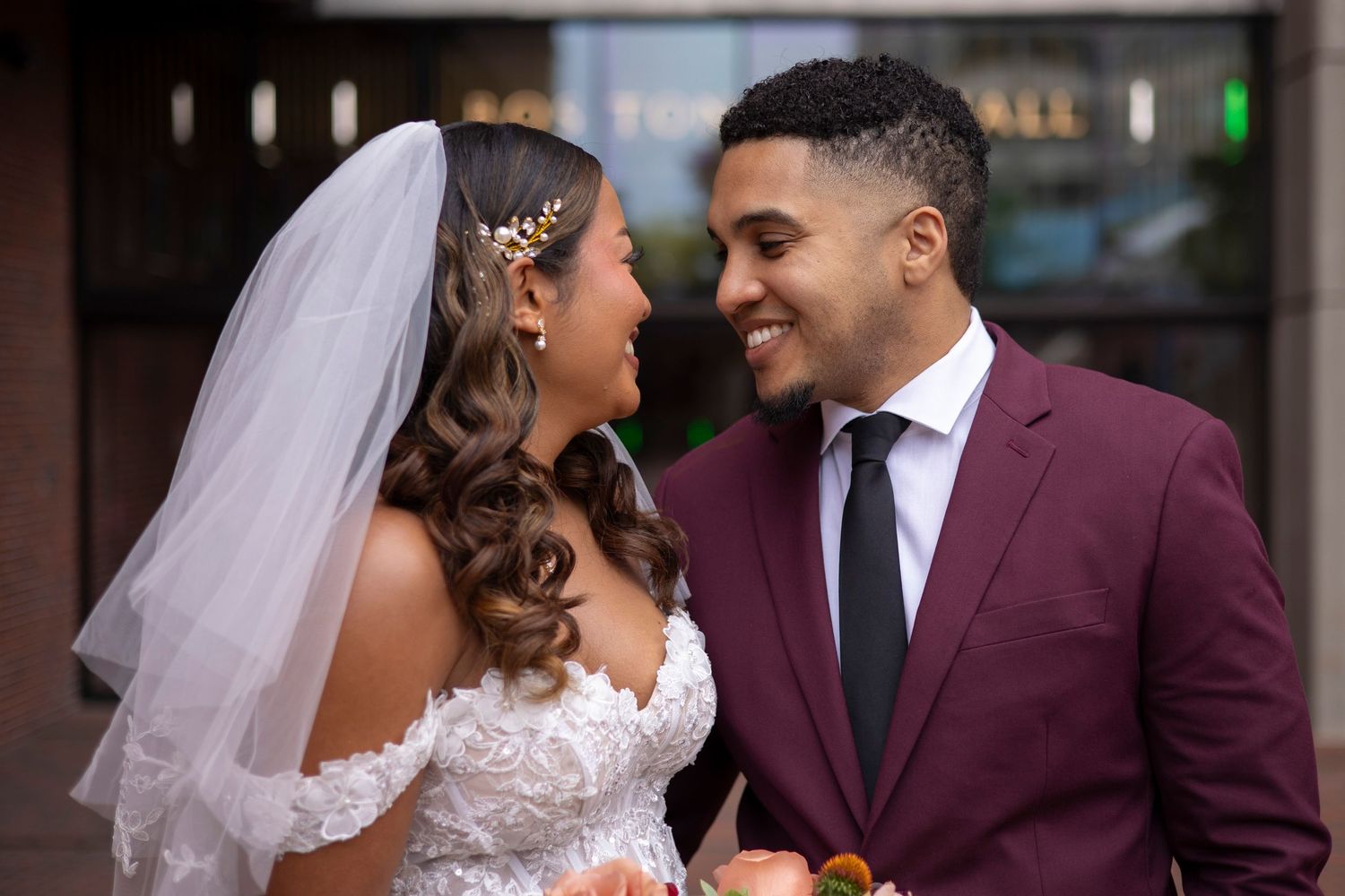 A bride and groom share an intimate moment together, with the bride in white lace and the groom in a burgundy suit.
