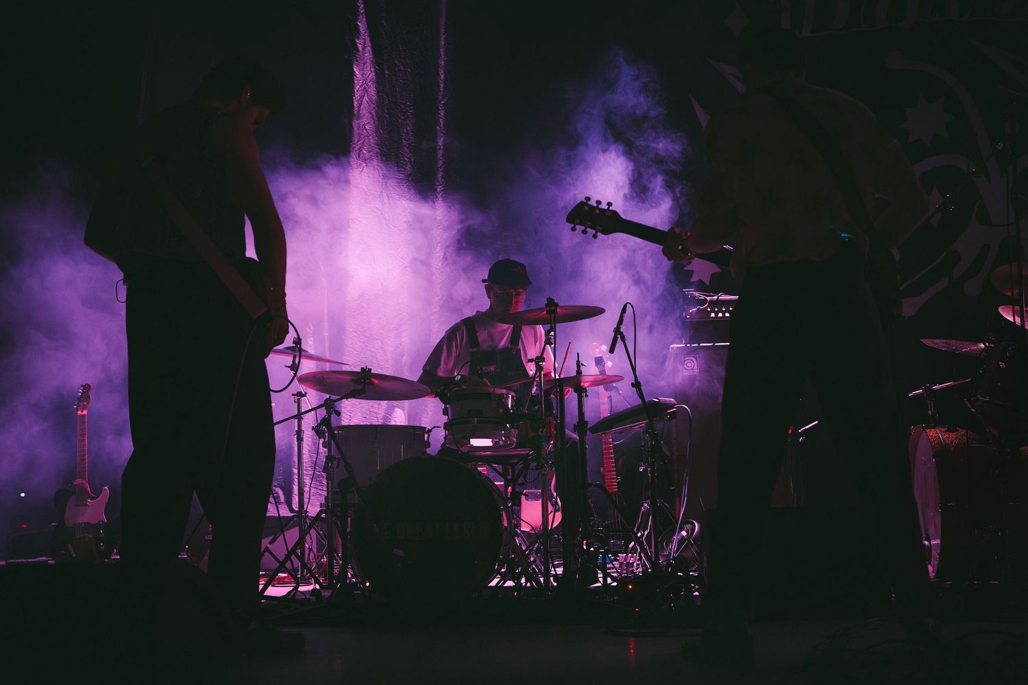 Performer in black clothing singing passionately on a dark stage with dramatic lighting.