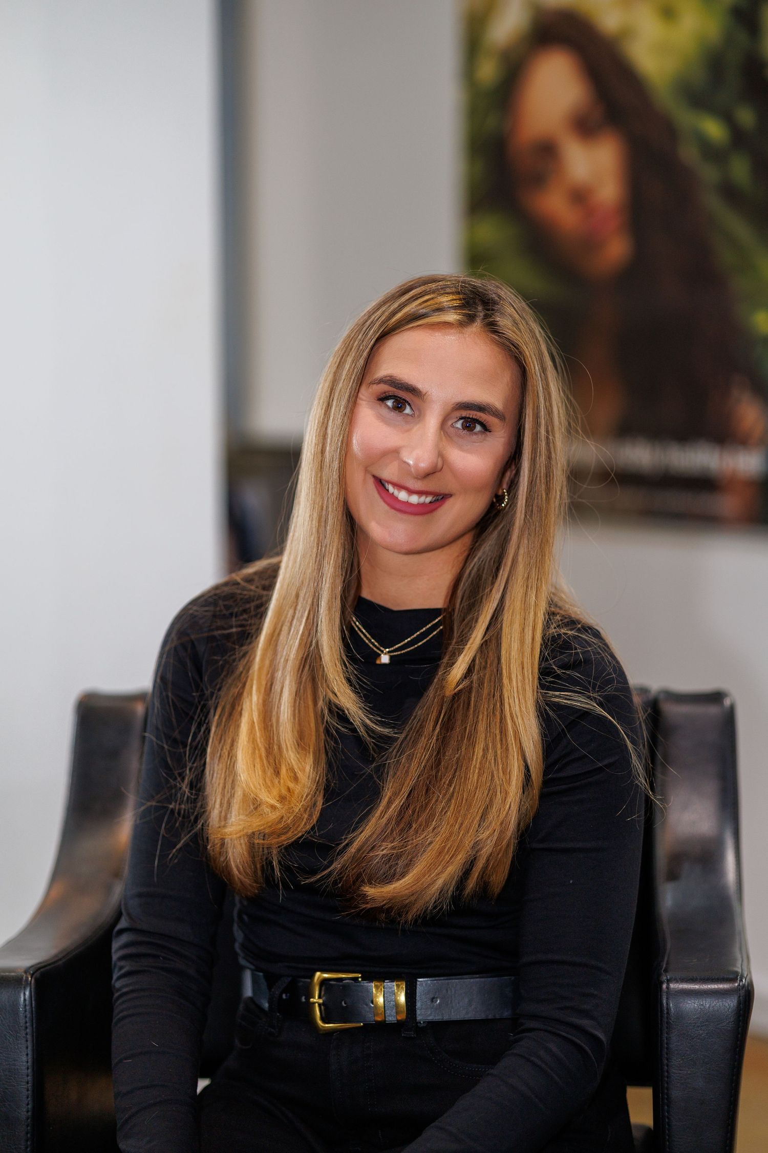 Person in black turtleneck sweater sitting in office chair with long blonde hair and warm smile.