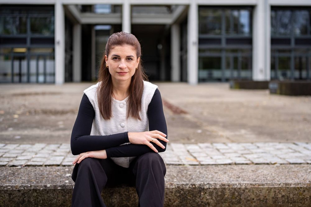 Professional woman in business attire sitting on steps outside an office building with a modern architectural backdrop.