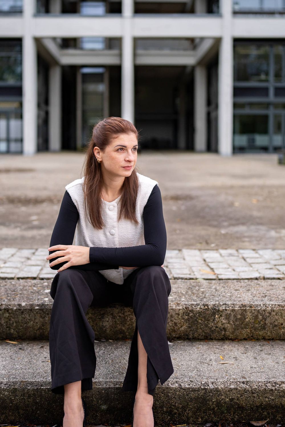 Professional wearing business attire sits thoughtfully on concrete steps outside a modern office building.