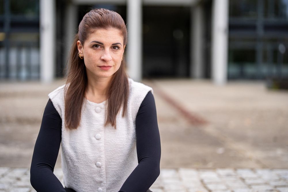Professional wearing a white blouse and navy blazer sits confidently in an urban business setting.