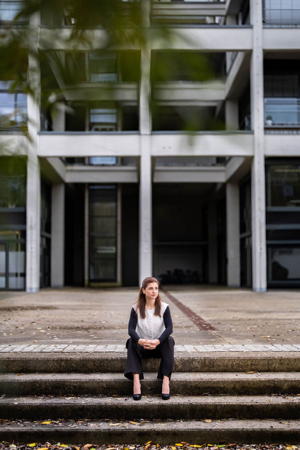 A person sits alone on concrete steps outside a modern office building with glass windows and columns.