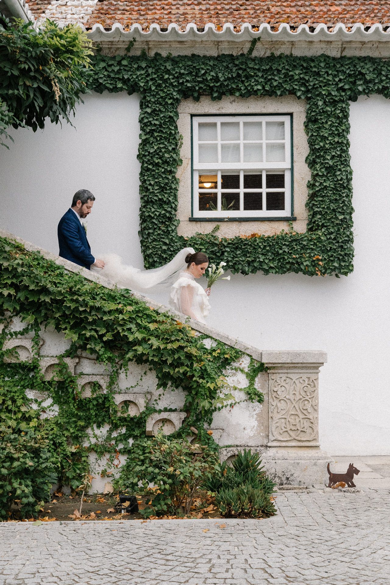 A sequence of photos showing a couple walking along an ivy-covered white wall with cobblestone ground and windows.