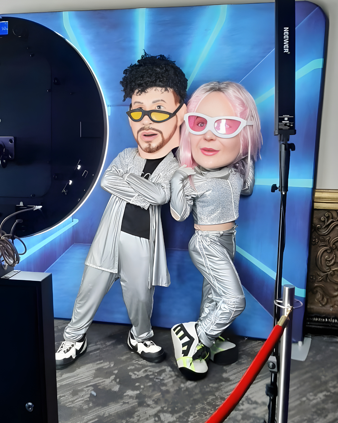Two people in matching silver and gray outfits pose playfully against a blue-lit backdrop during a photoshoot.