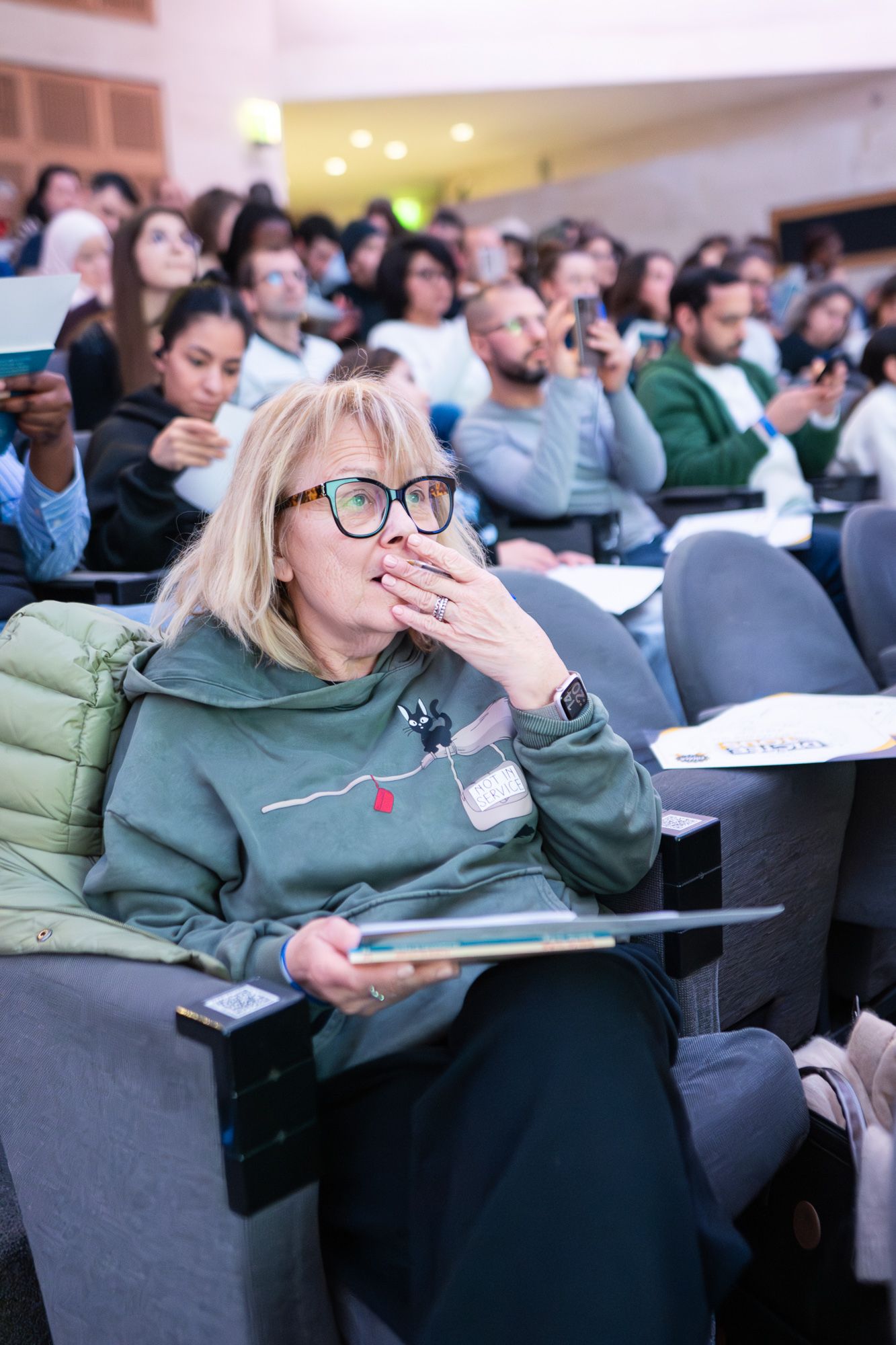 Student yawns while taking notes during a crowded lecture in an academic classroom setting.