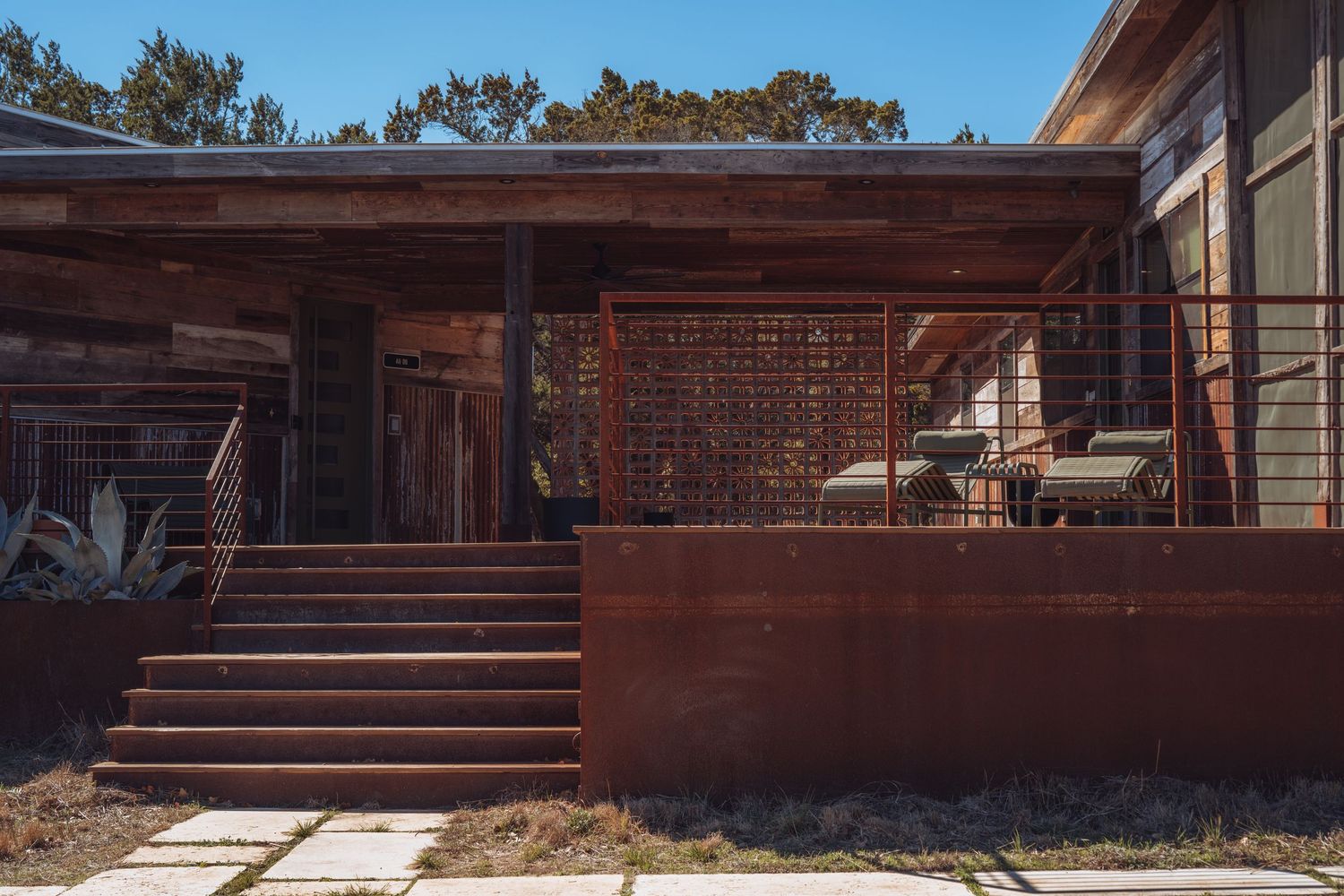 Modern wooden deck with horizontal railings extends along red brick house exterior under forest canopy.