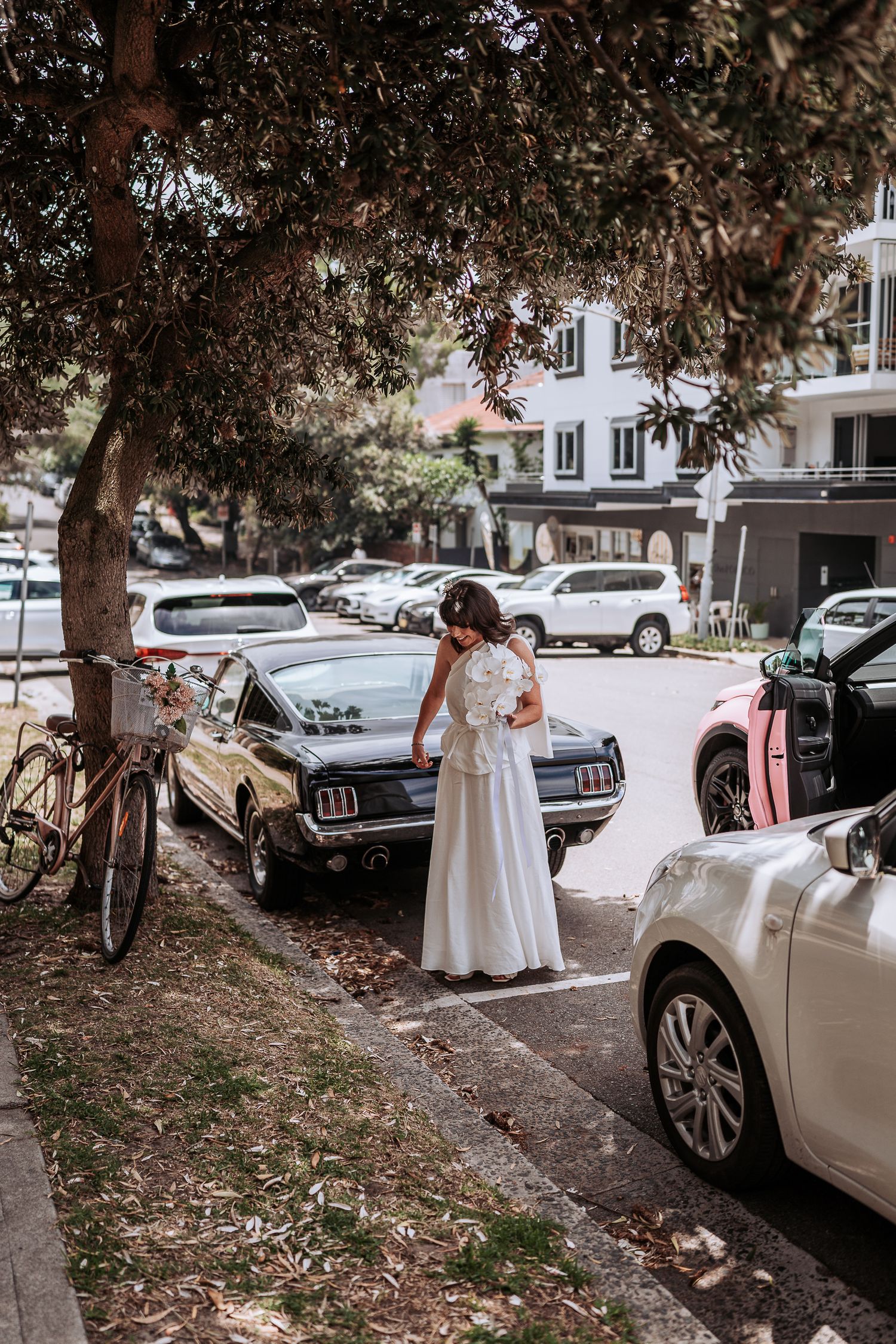 White vintage car parked on a tree-lined street during a wedding celebration.
