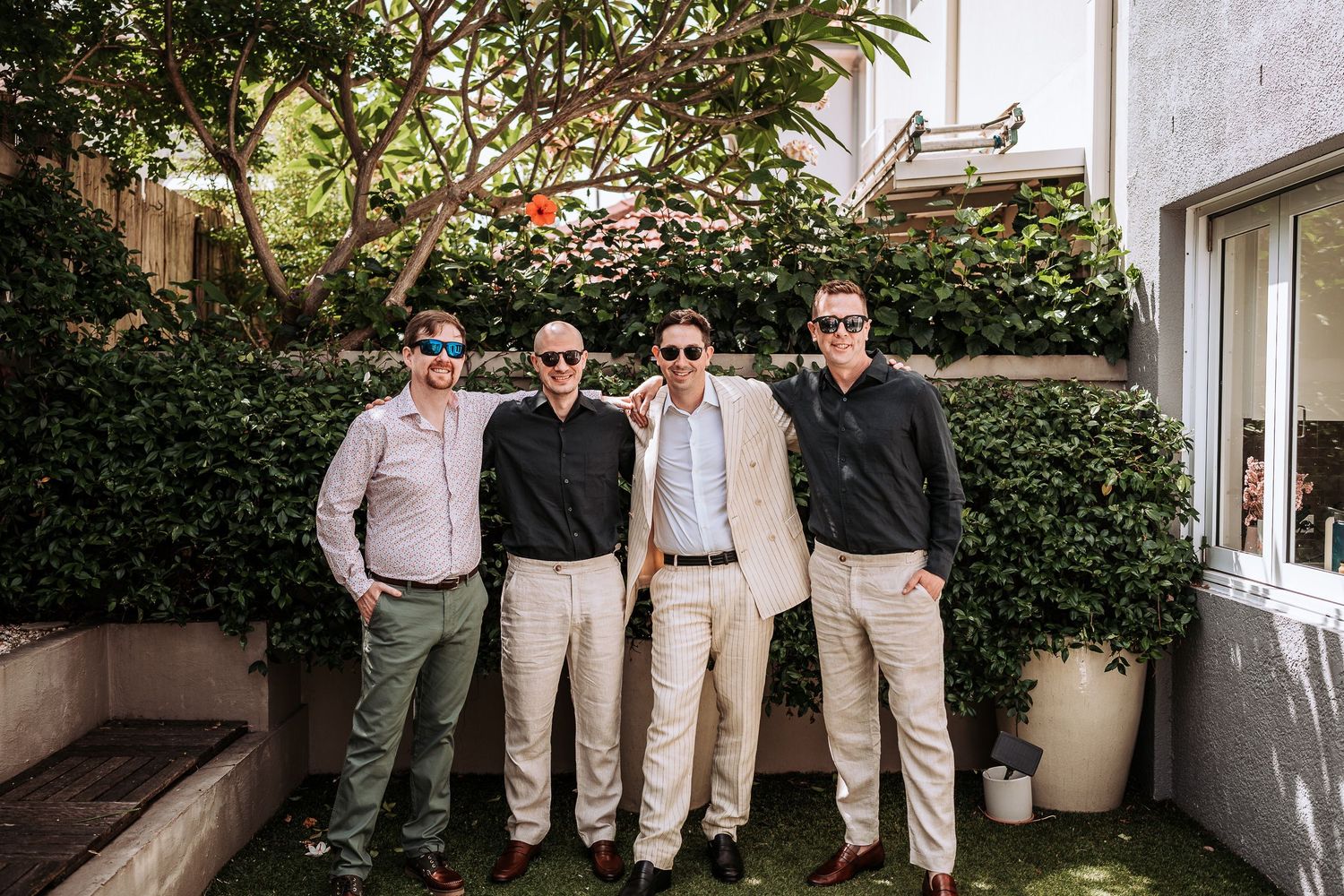 Wedding party in coordinated beige and white outfits pose together outside a building.