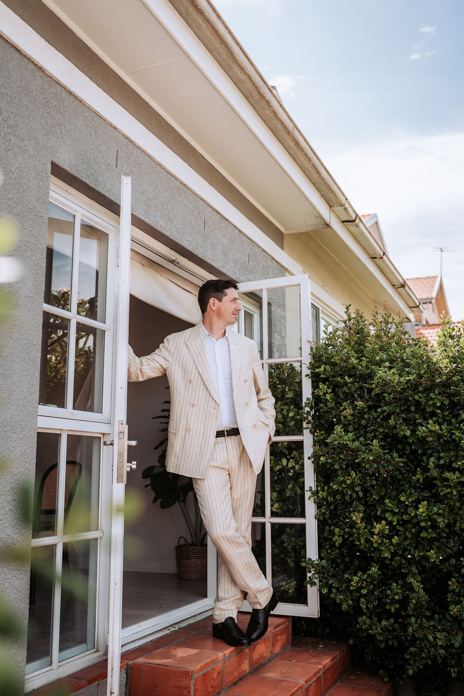Series of photos showing someone climbing through a window of a house with white trim and green bushes outside.