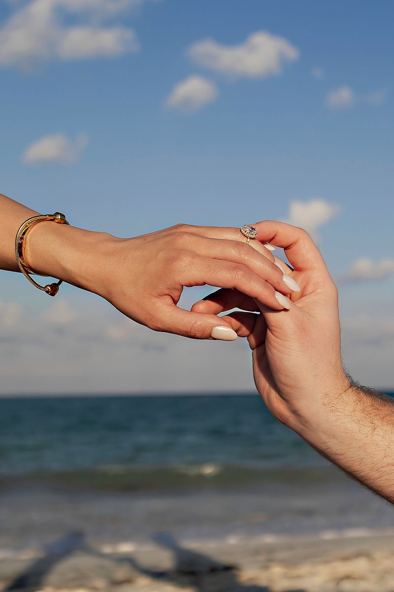 Close-up sequence of hands exchanging rings during a beach wedding ceremony with ocean and blue sky in background.
