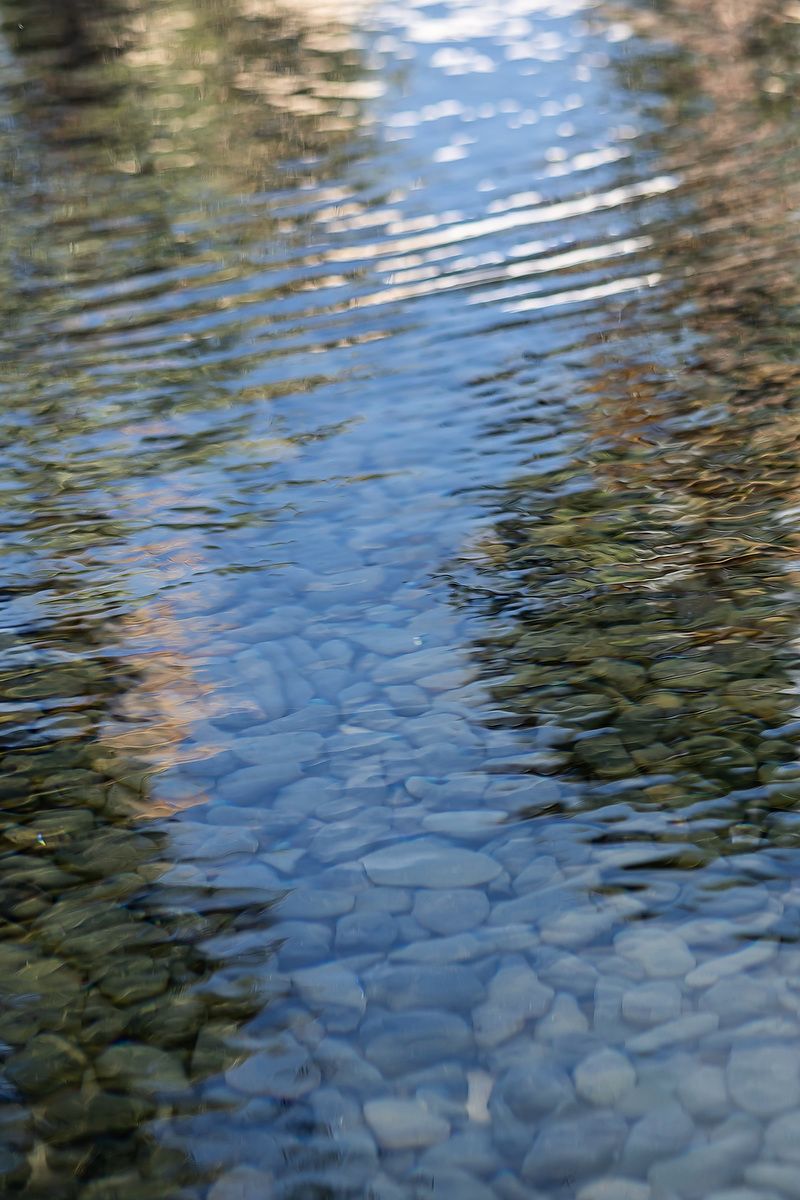 Rippling water surface reveals smooth stones beneath with sunlight reflections creating a tranquil aquatic scene.