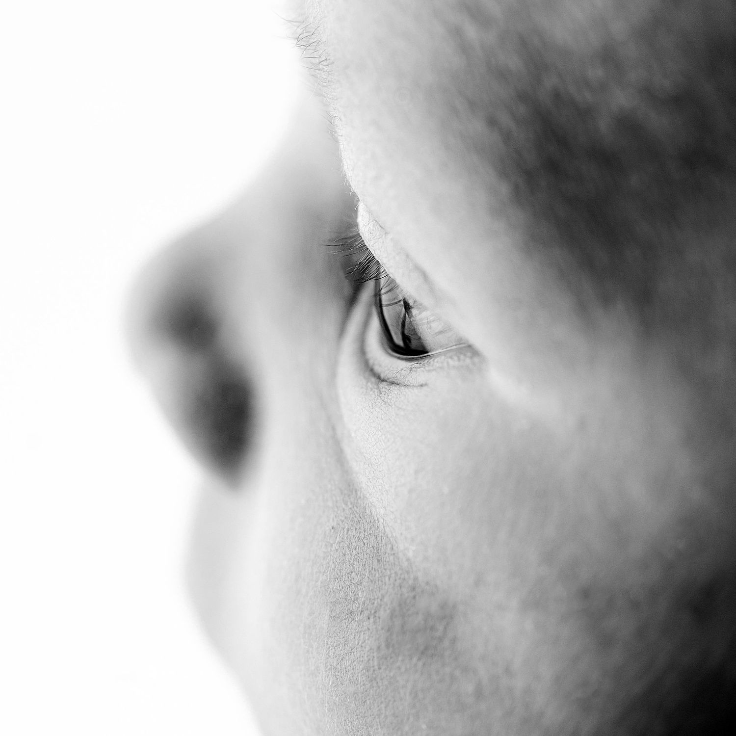Close-up black and white portrait showing a partial view of someone's eye and nose in soft focus.