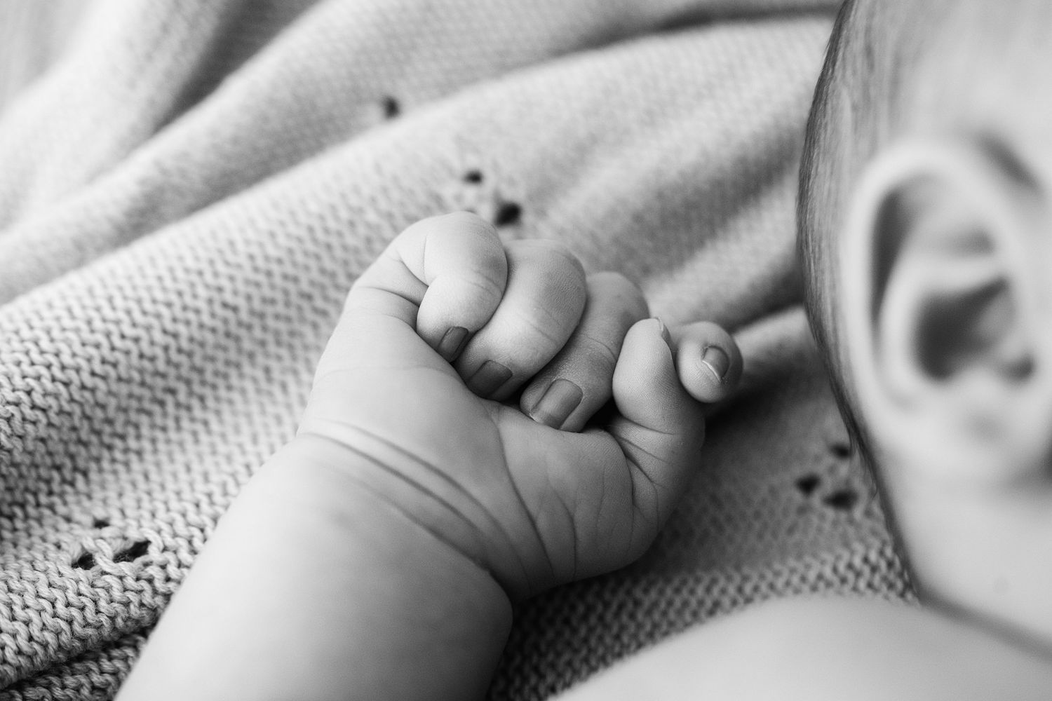 Close-up black and white photo of a baby's tiny hand grasping an adult's finger in a tender moment.