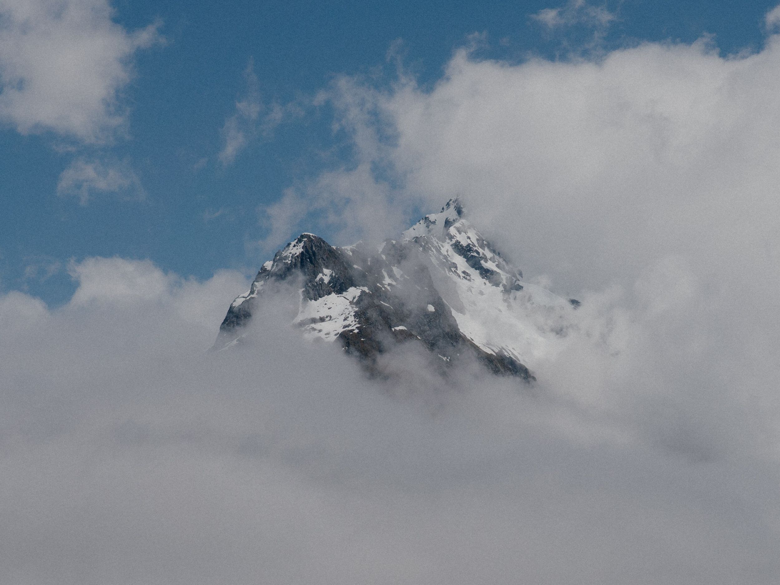 Dramatic mountain peak emerging through misty clouds against a blue sky.