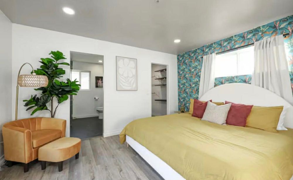 Modern studio apartment interior with light wood floors, blue floral wallpaper, and white furnishings.