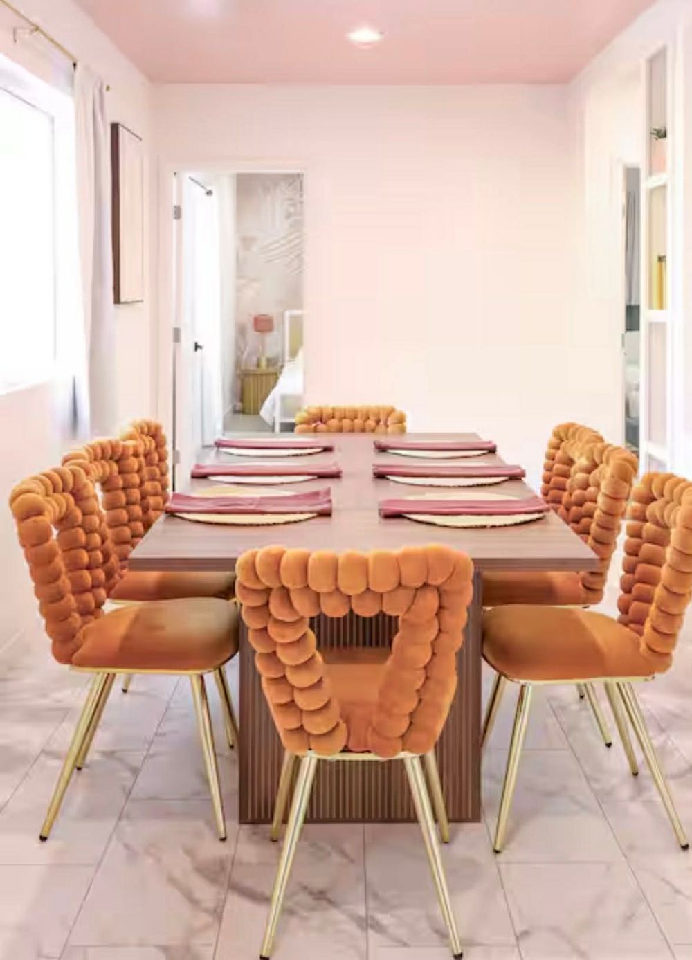 Modern dining room with plush velvet orange chairs and white table set for a formal dinner on marble flooring.