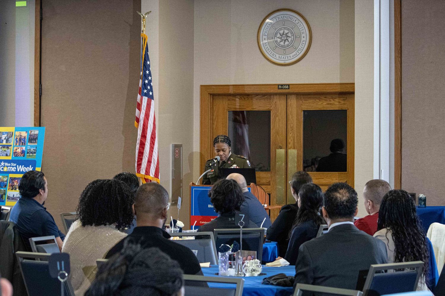 Speaker presenting to an audience in a room decorated with American flag.