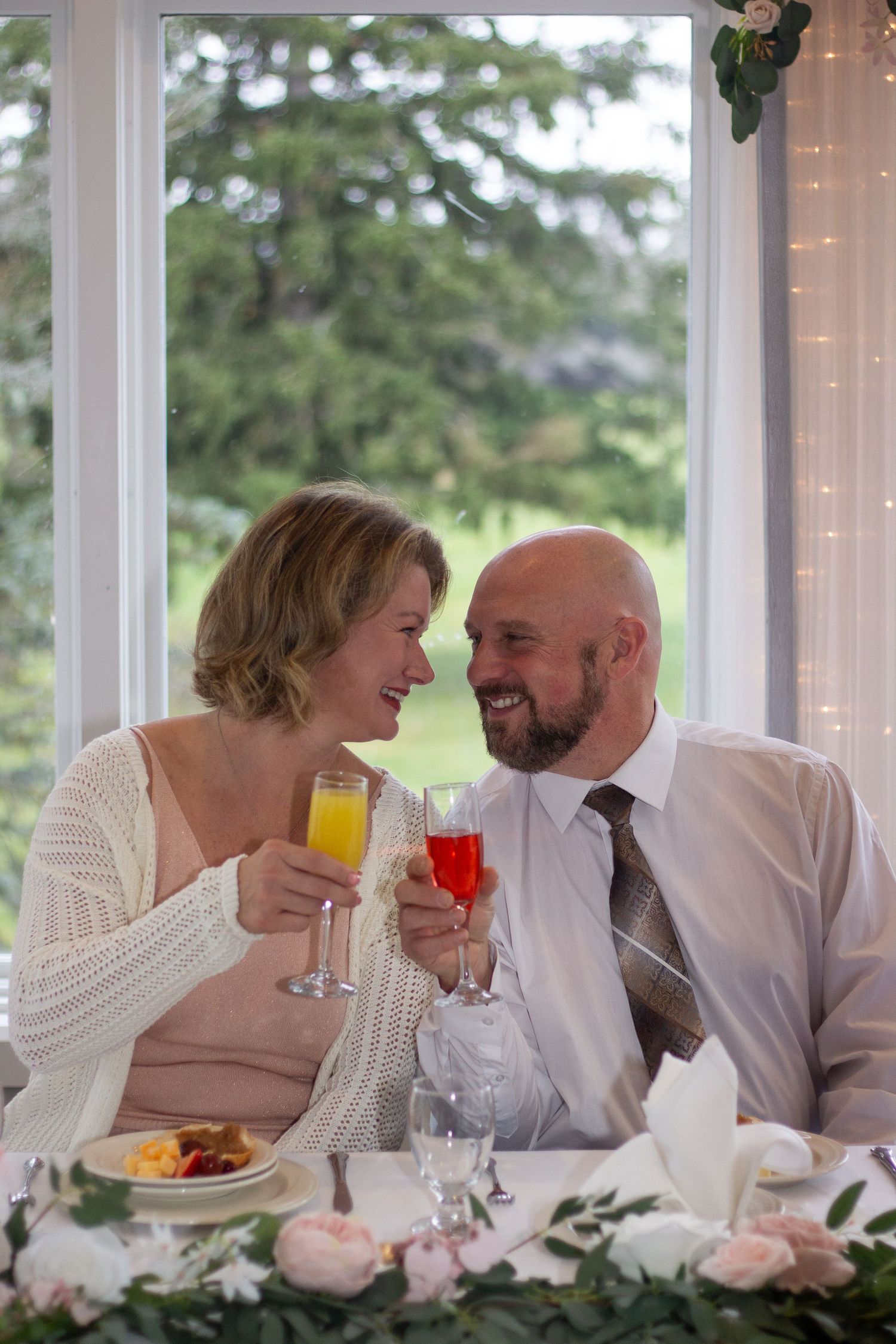 A couple shares an intimate moment at a wedding reception table decorated with white linens and floral arrangements.