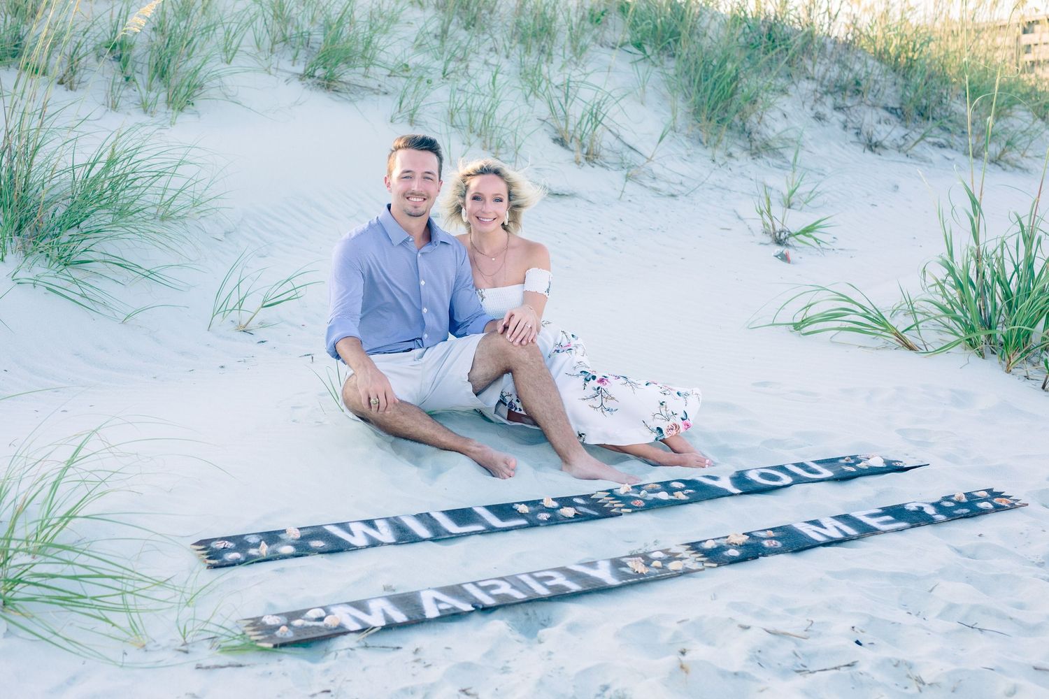Newly engaged couple laughing and embracing sitting on the scenic beach, Windsor Ontario, captured by Tasha Cannaday.