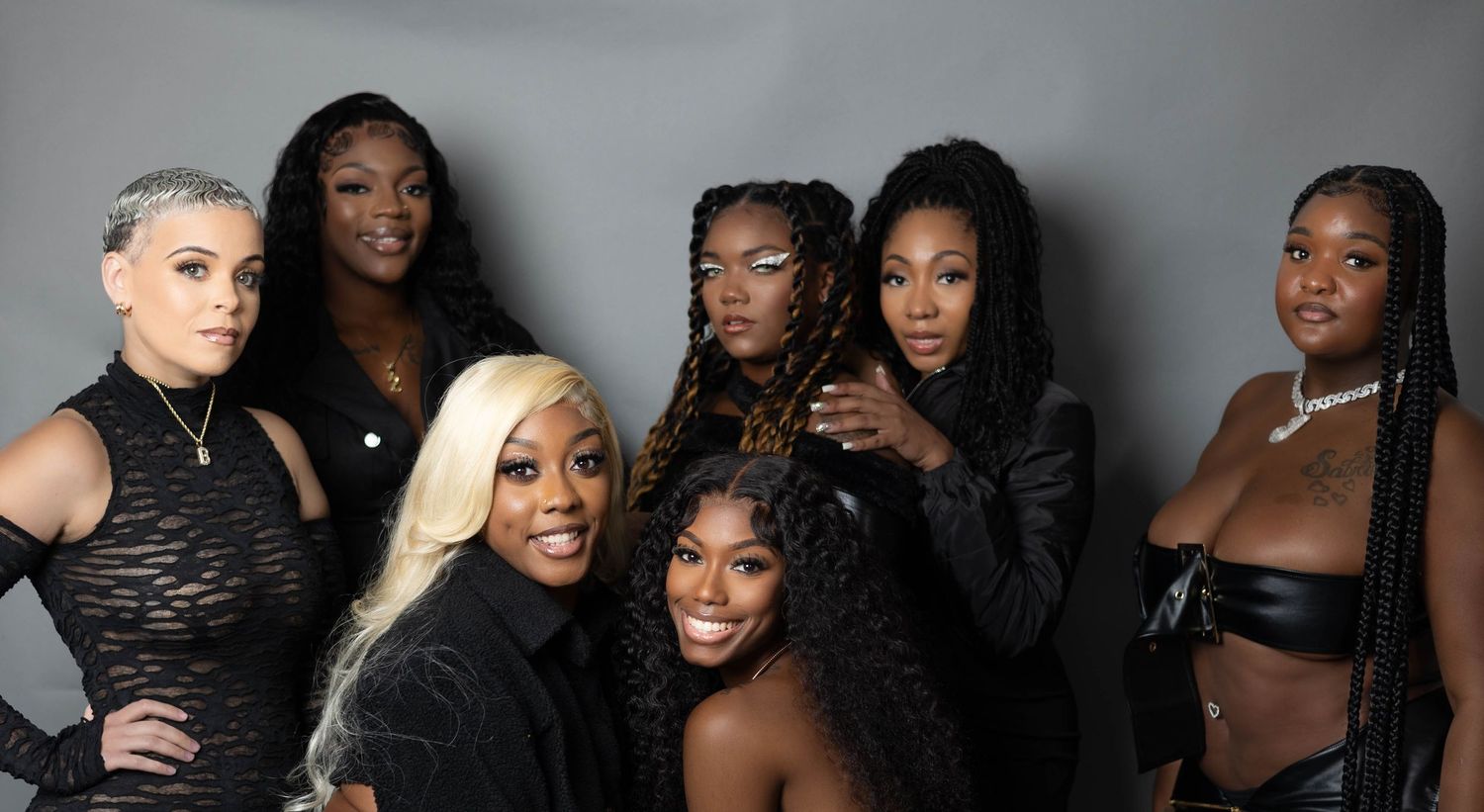 Group of seven stylish women posing together in black outfits for a professional photo shoot.