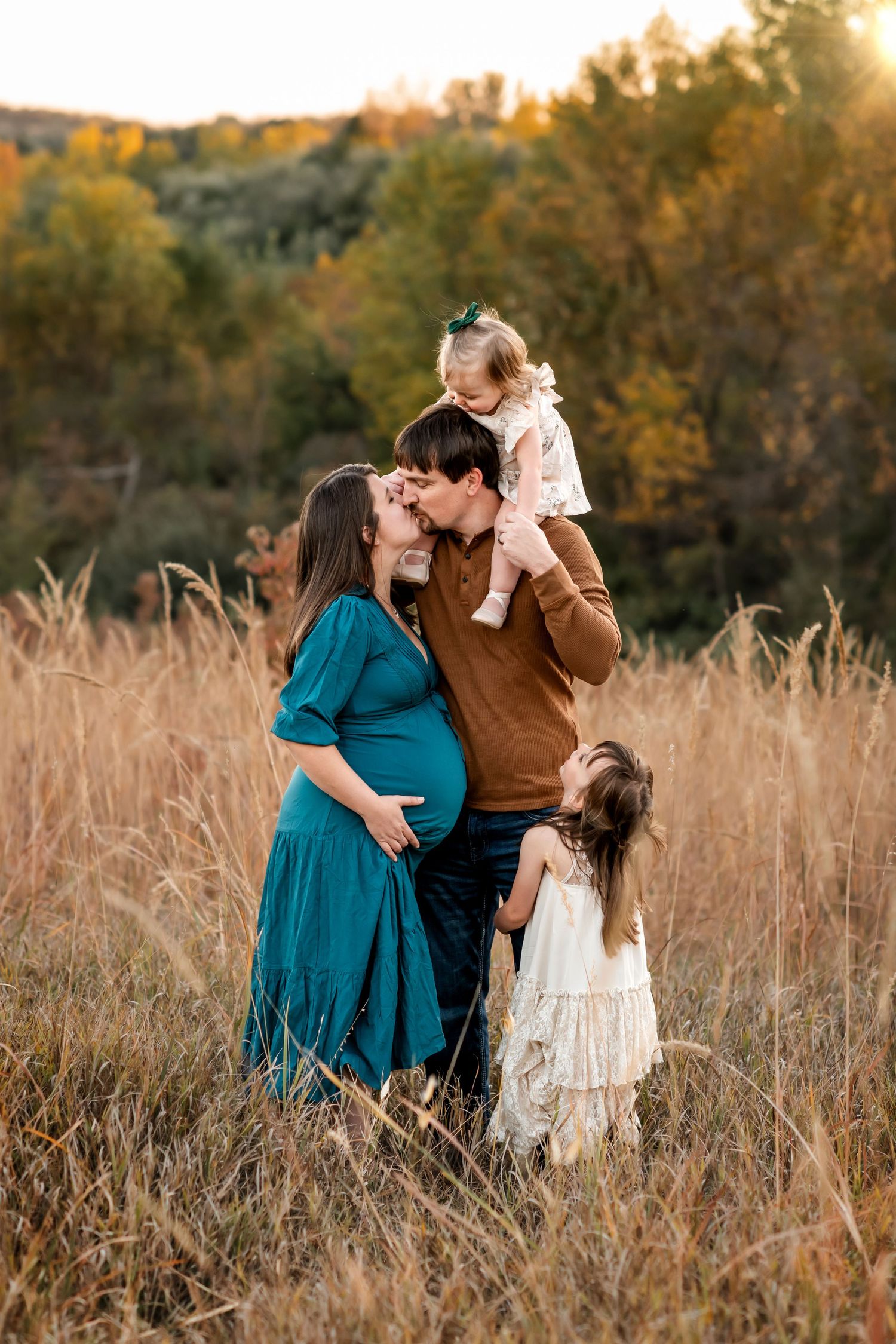 A family moment captured in tall grass during golden hour with fall foliage behind them.