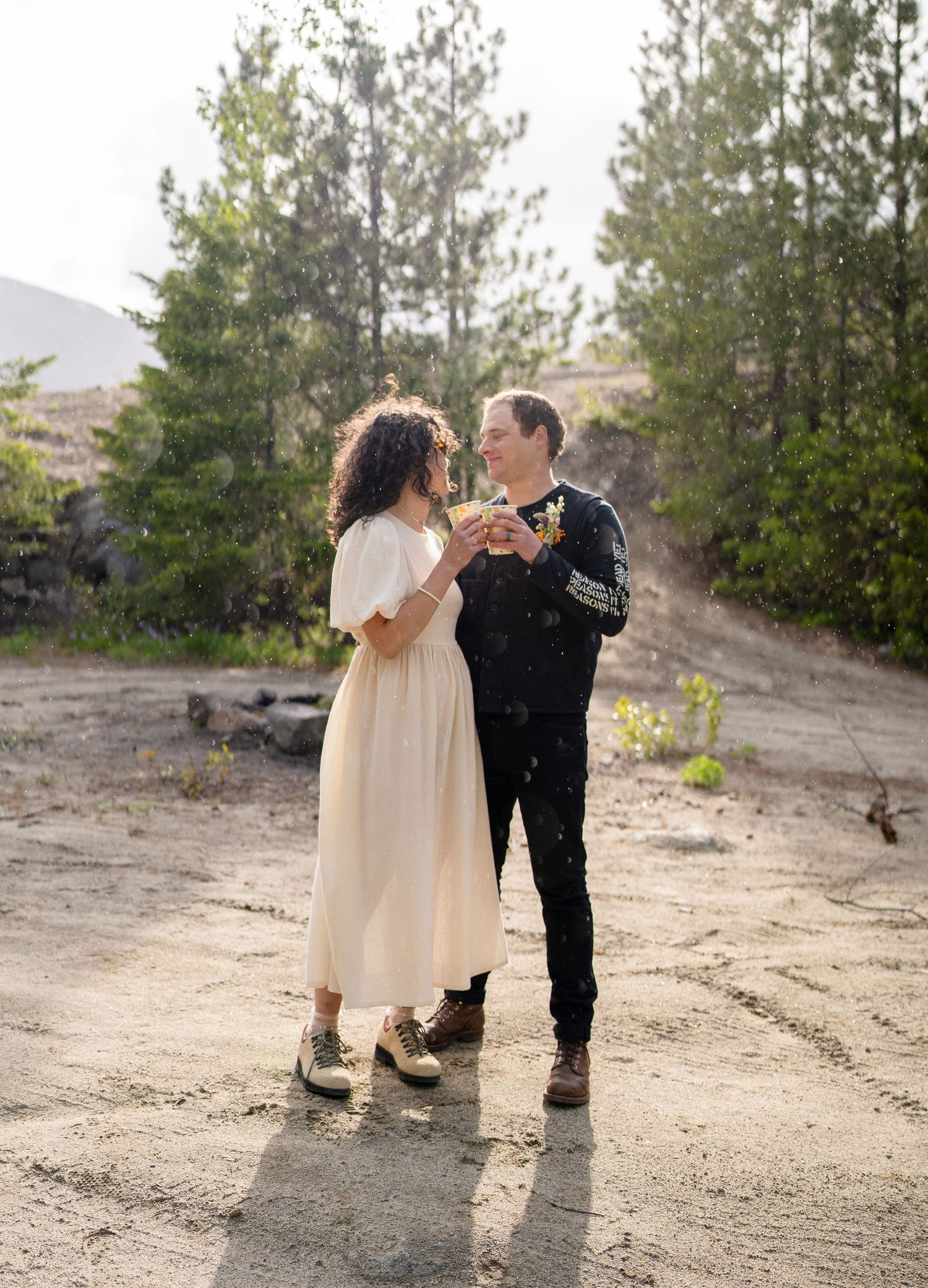 Couple shares intimate moment on dirt path surrounded by pine trees.