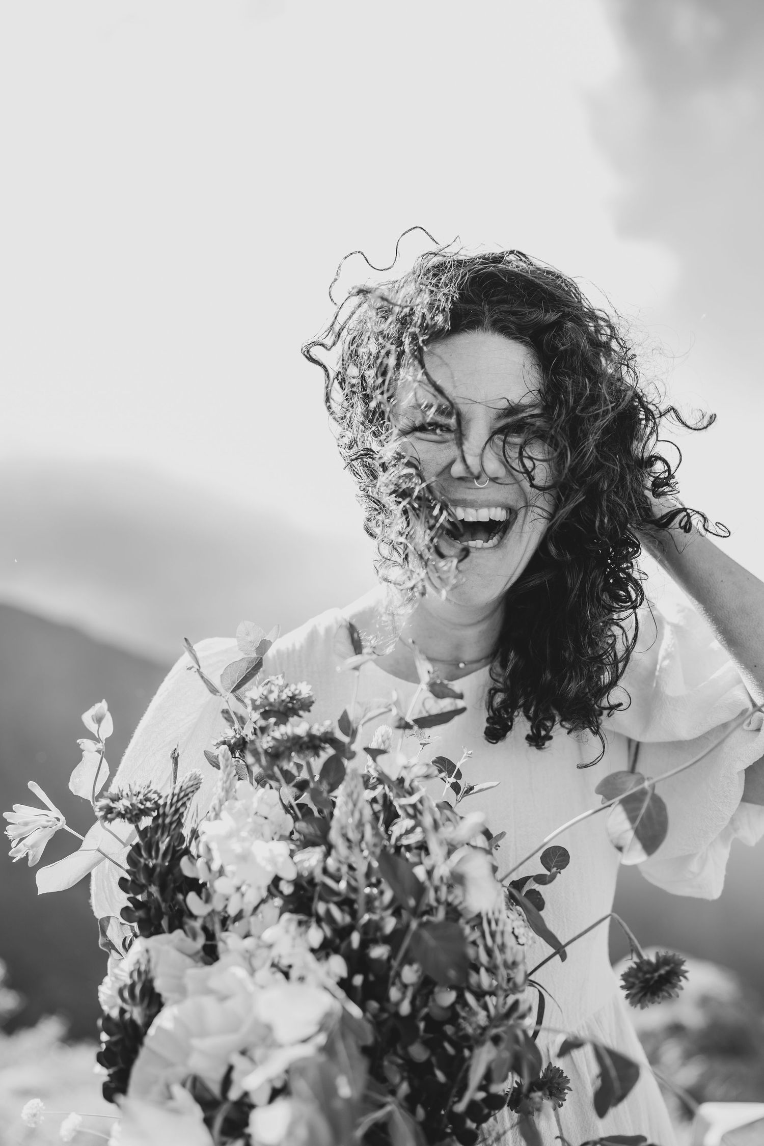 Black and white portrait with floral bouquet against outdoor mountains.