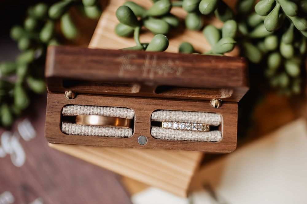 Two wedding rings nestled in wooden box with decorative greenery.