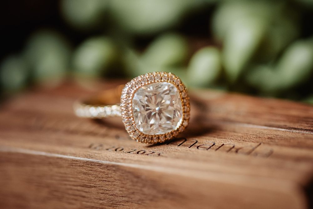 Elegant cushion-cut diamond engagement ring with halo setting on wooden surface.