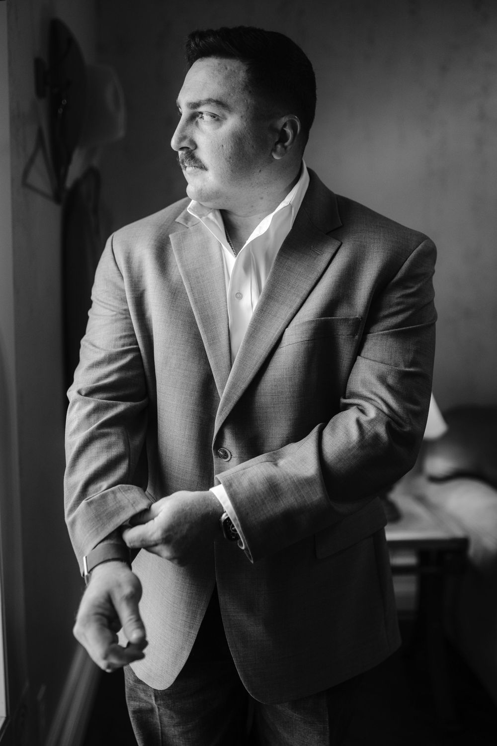 Man in grey suit jacket looking to the side in dramatic black and white portrait.
