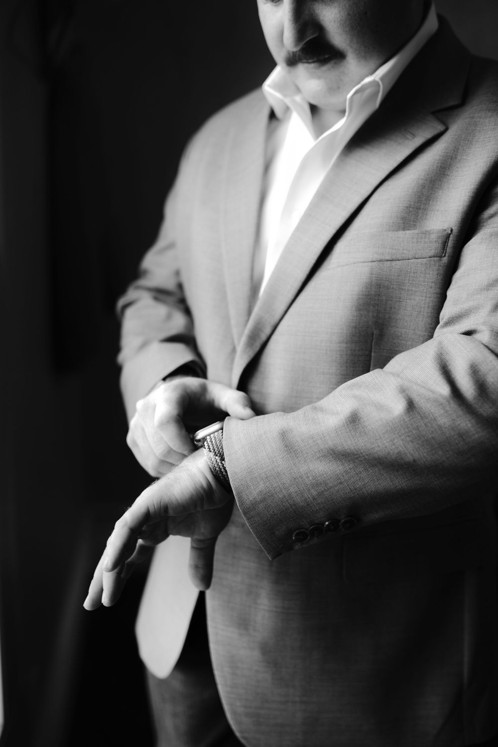 Black and white close-up of person adjusting sleeve of grey suit jacket.