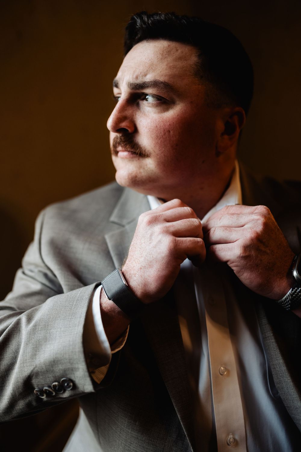 Man in grey suit adjusting tie in dramatic lighting portrait shot.