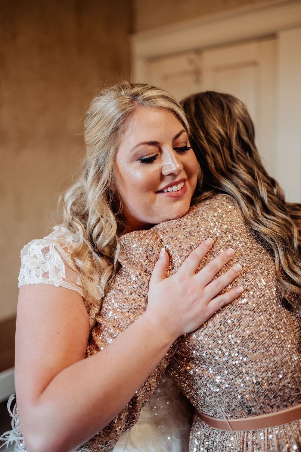 Two people sharing an emotional embrace, one wearing a white dress and one in sparkly gold.
