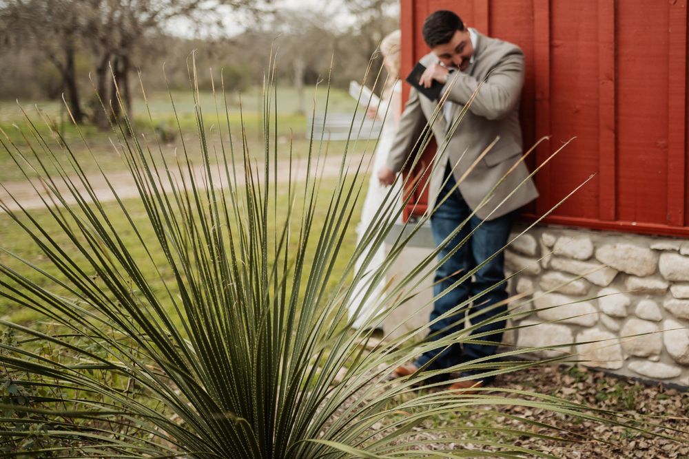 Wedding photographer taking pictures near red building with desert plants.