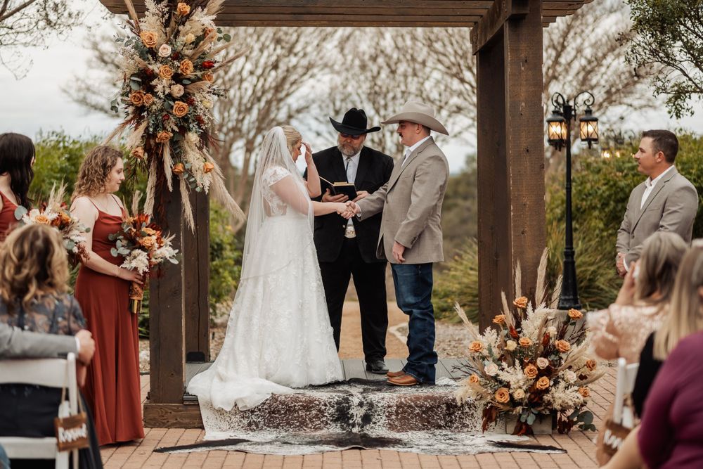 Outdoor wedding ceremony under wooden pergola with autumn-colored floral arrangements.