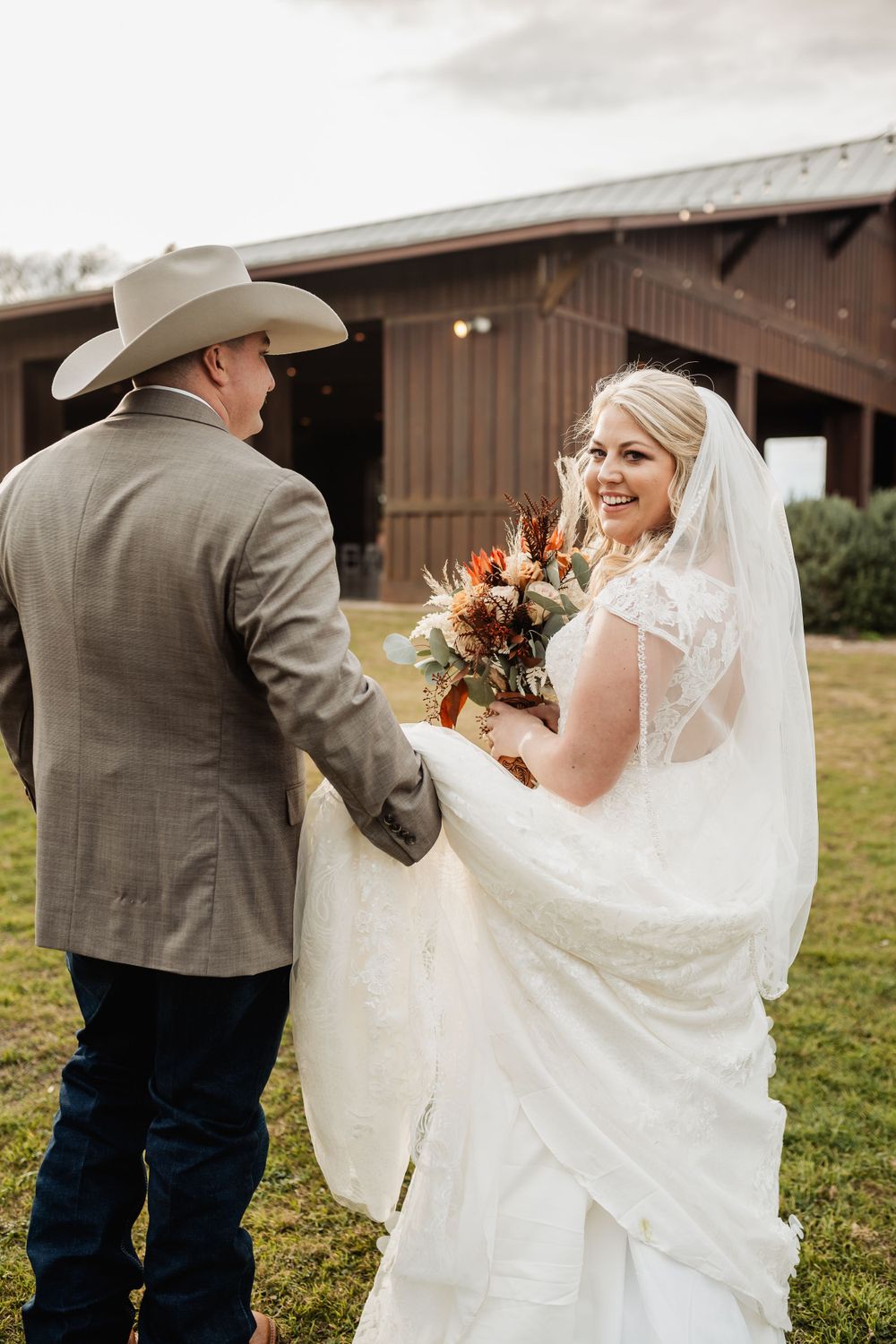 Western-style wedding couple sharing a moment outside a rustic barn with autumn bouquet.