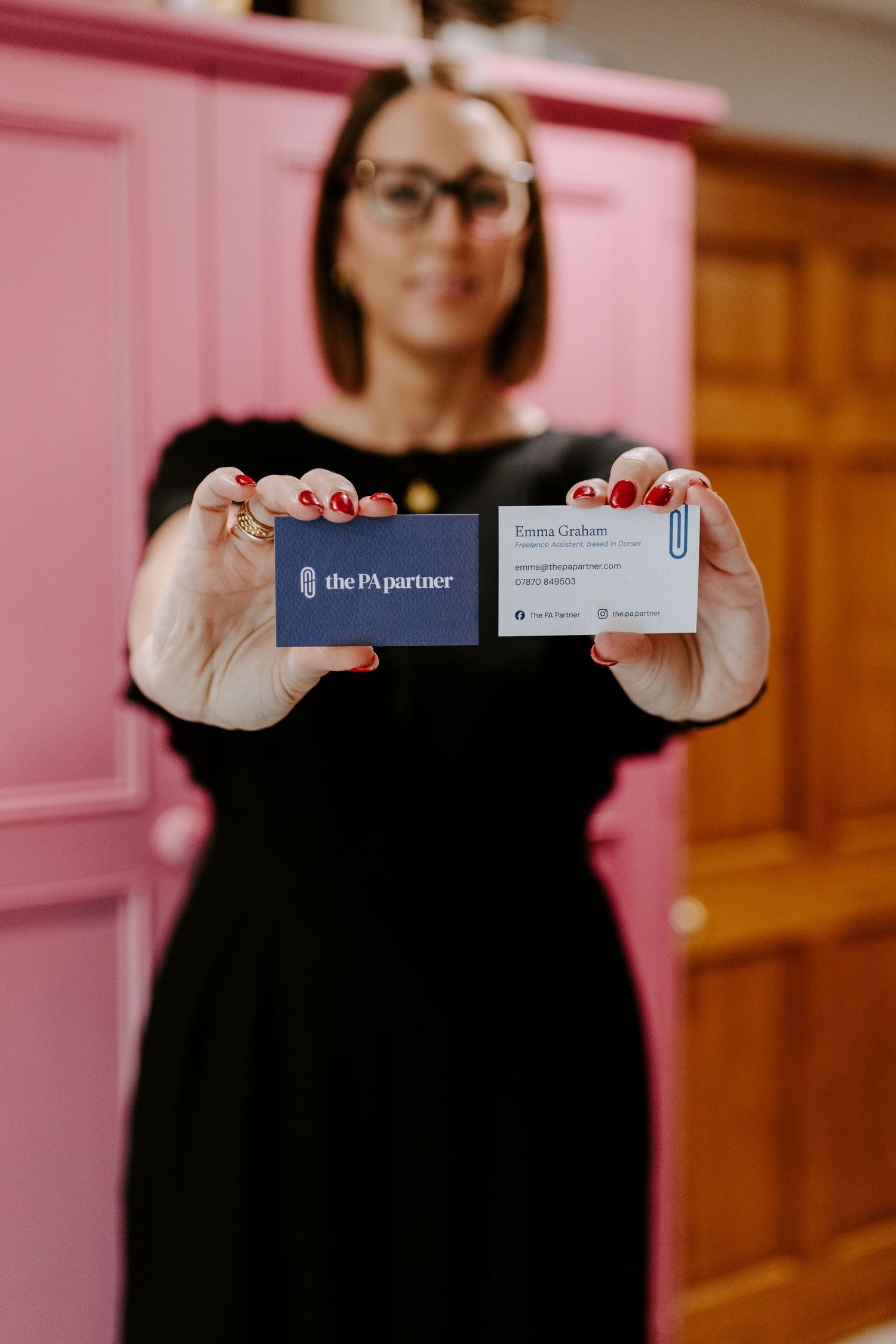 Professional holding up business cards against a pink wall in a series of closeup shots.