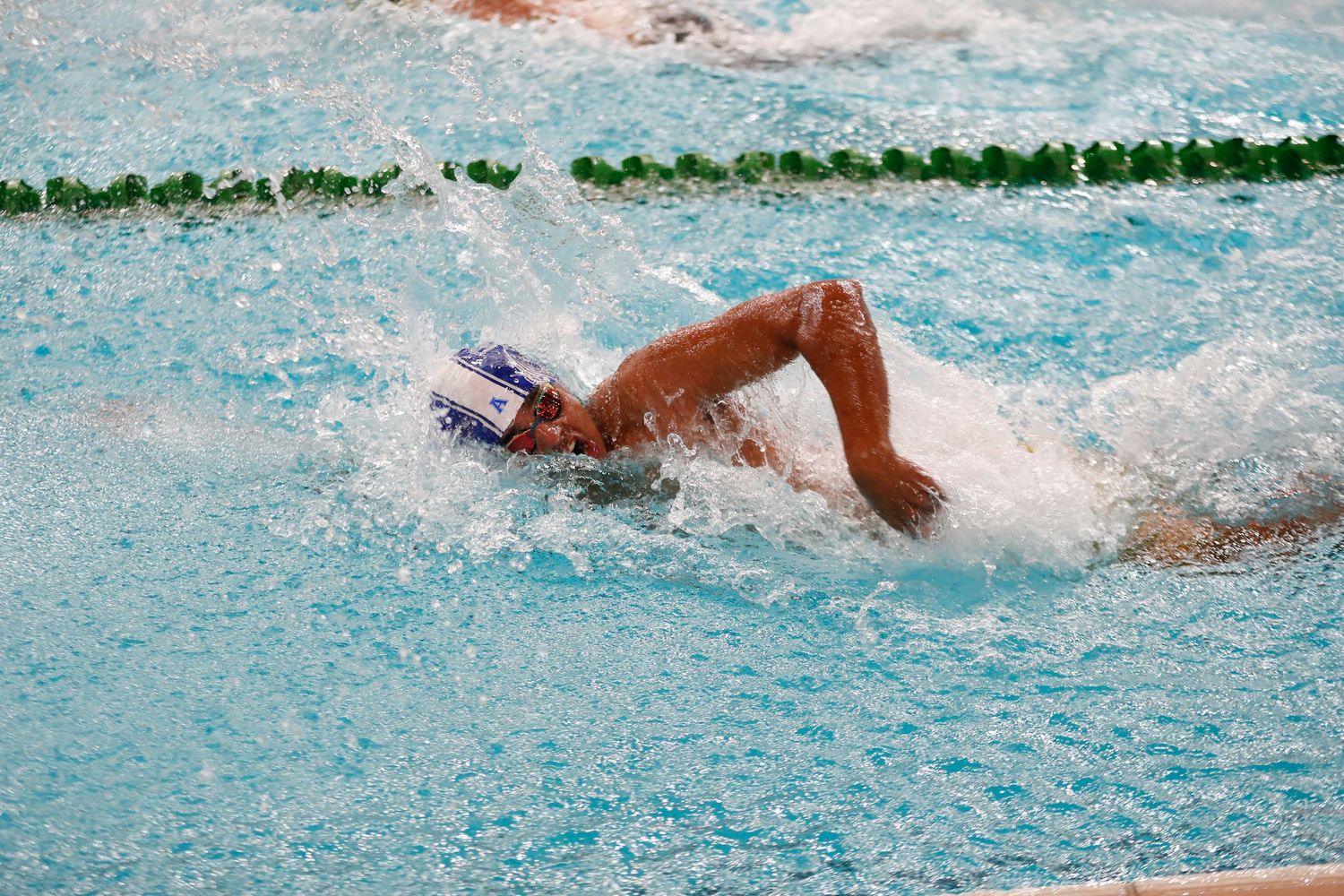 Swimmer performing freestyle stroke in competition pool with splashing water.