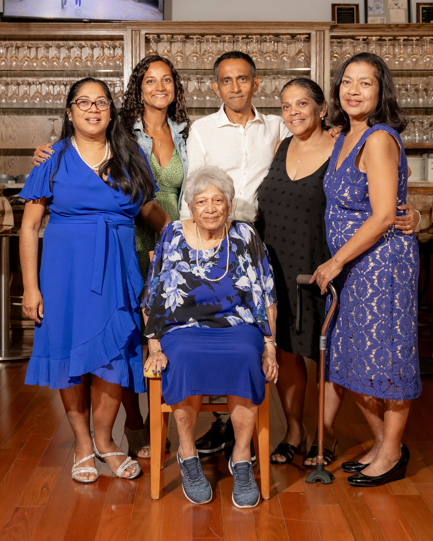 A multigenerational family gathering poses together in formal attire in front of a bar display.