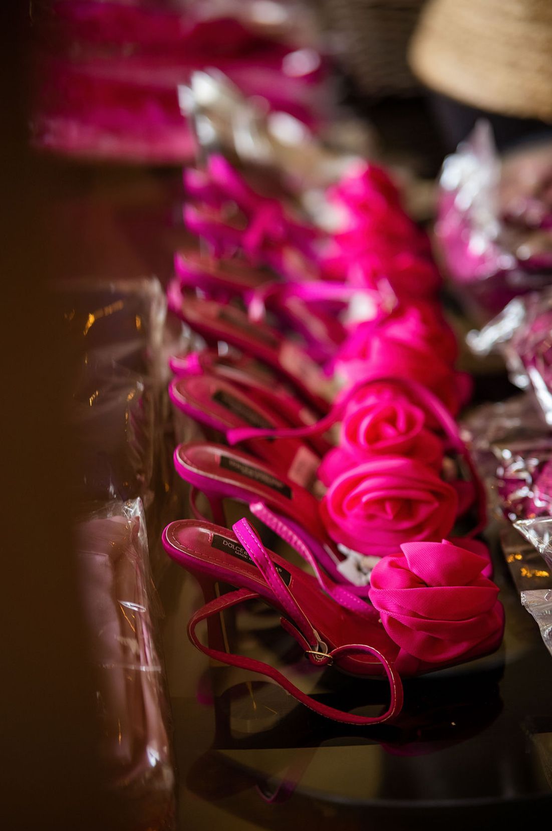 A row of bright pink high-heeled sandals with rose decorations lined up on display in soft lighting.