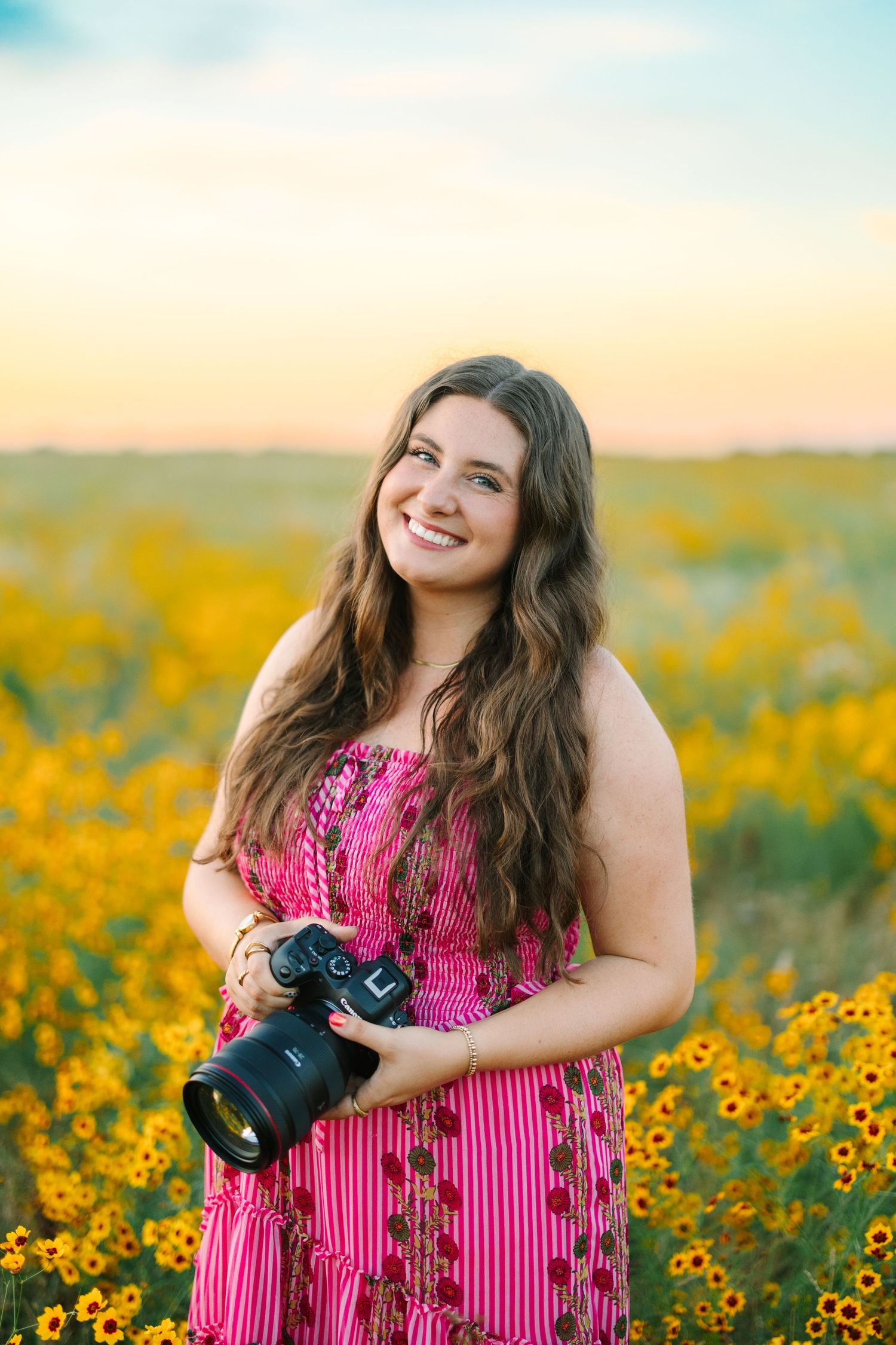 Professional photographer in mint green top holding camera gear with joyful expression against white background.
