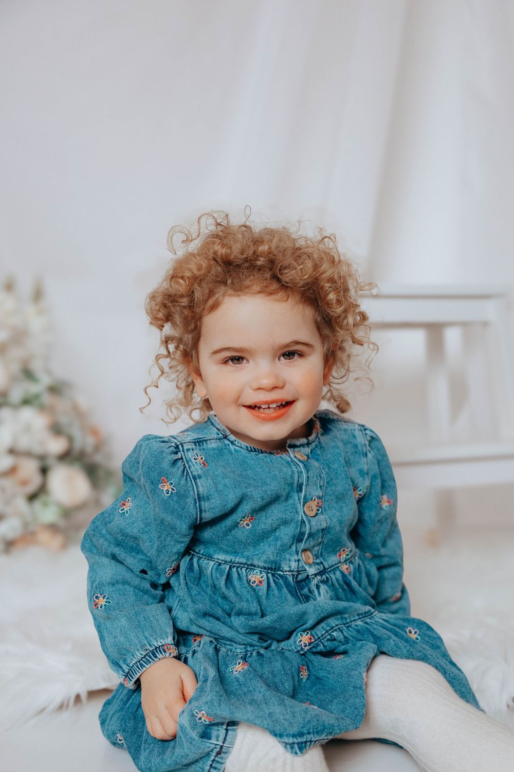 Close up portrait of smiling child in blue denim dress against white background.