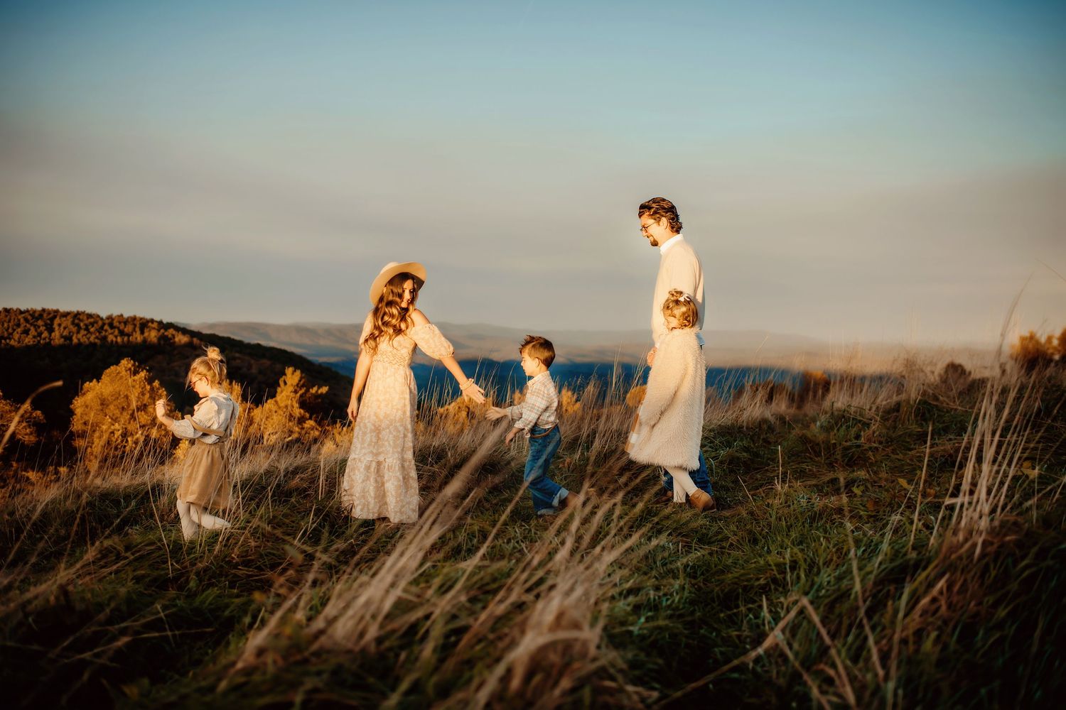 A group in white dresses walks through a sunlit meadow at golden hour with tall grass swaying in the breeze.