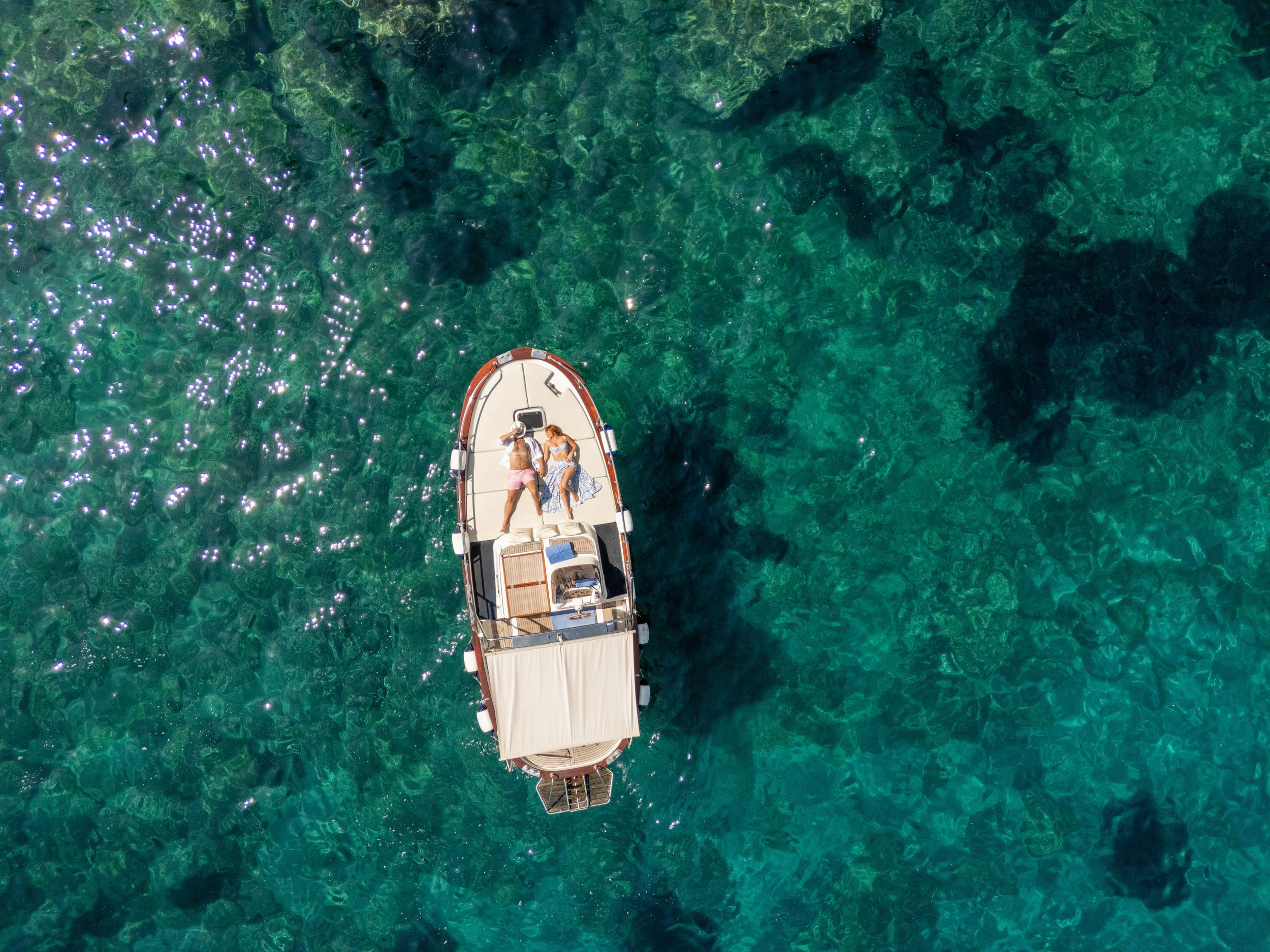 Aerial view of a small boat floating on crystal clear turquoise waters surrounded by coral reefs.