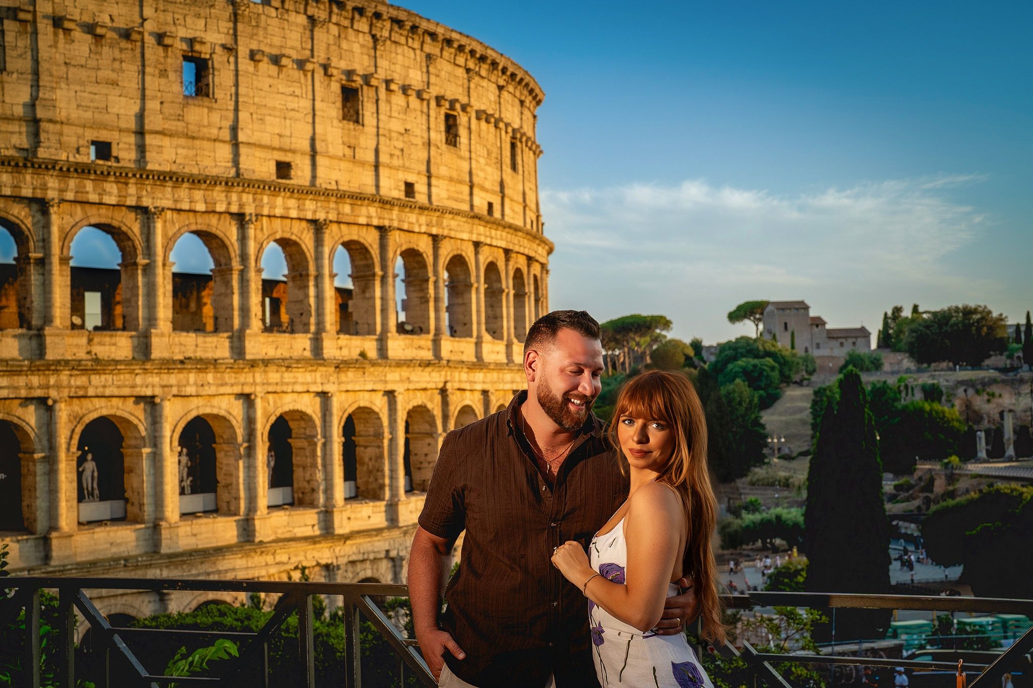 A couple poses together in front of the historic Colosseum in Rome, Italy during golden hour.